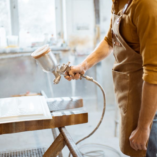 Worker painting wooden product with a spray gun at the painting shop of the carpentry